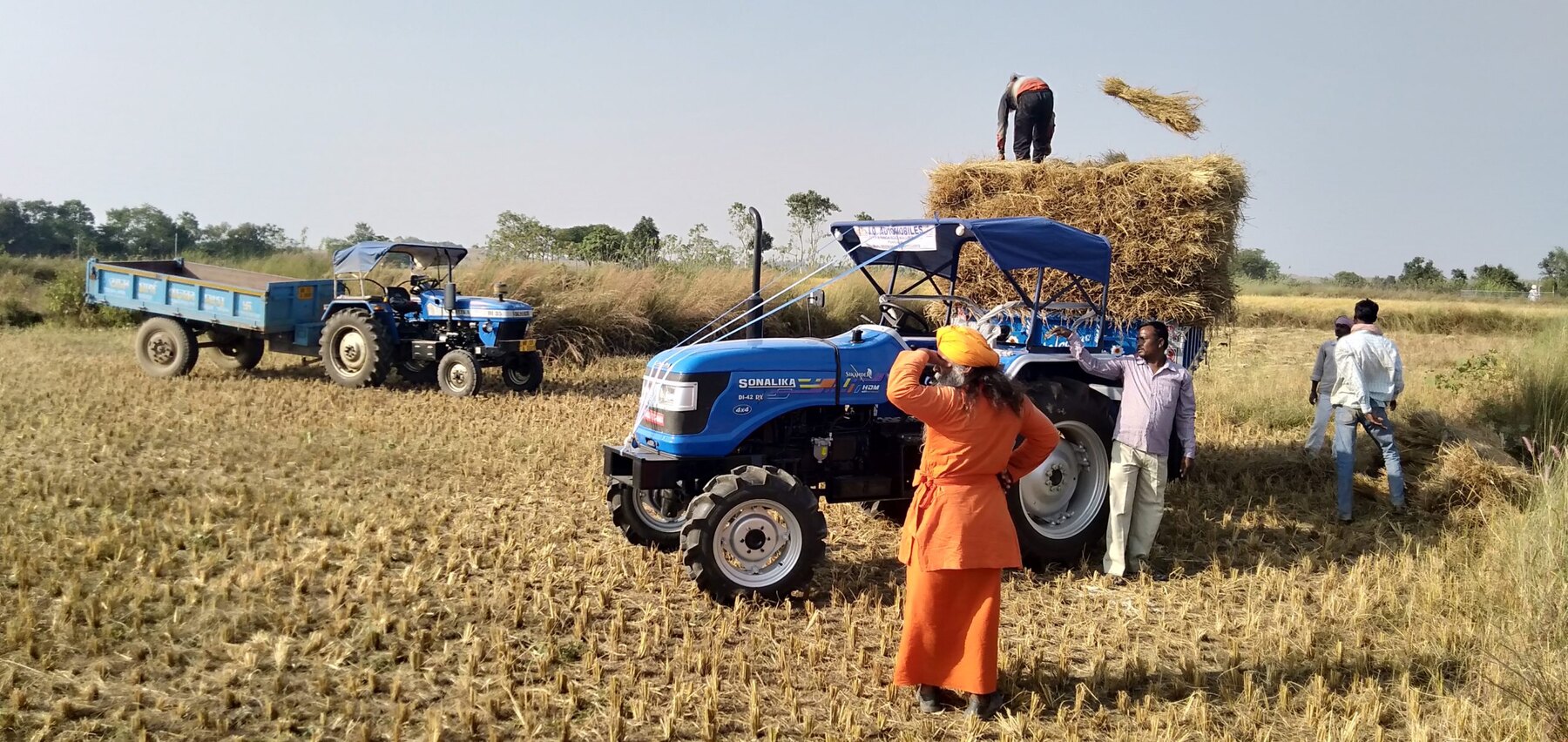 A tractor and farm workers gathering the harvest at Ánanda Nagar